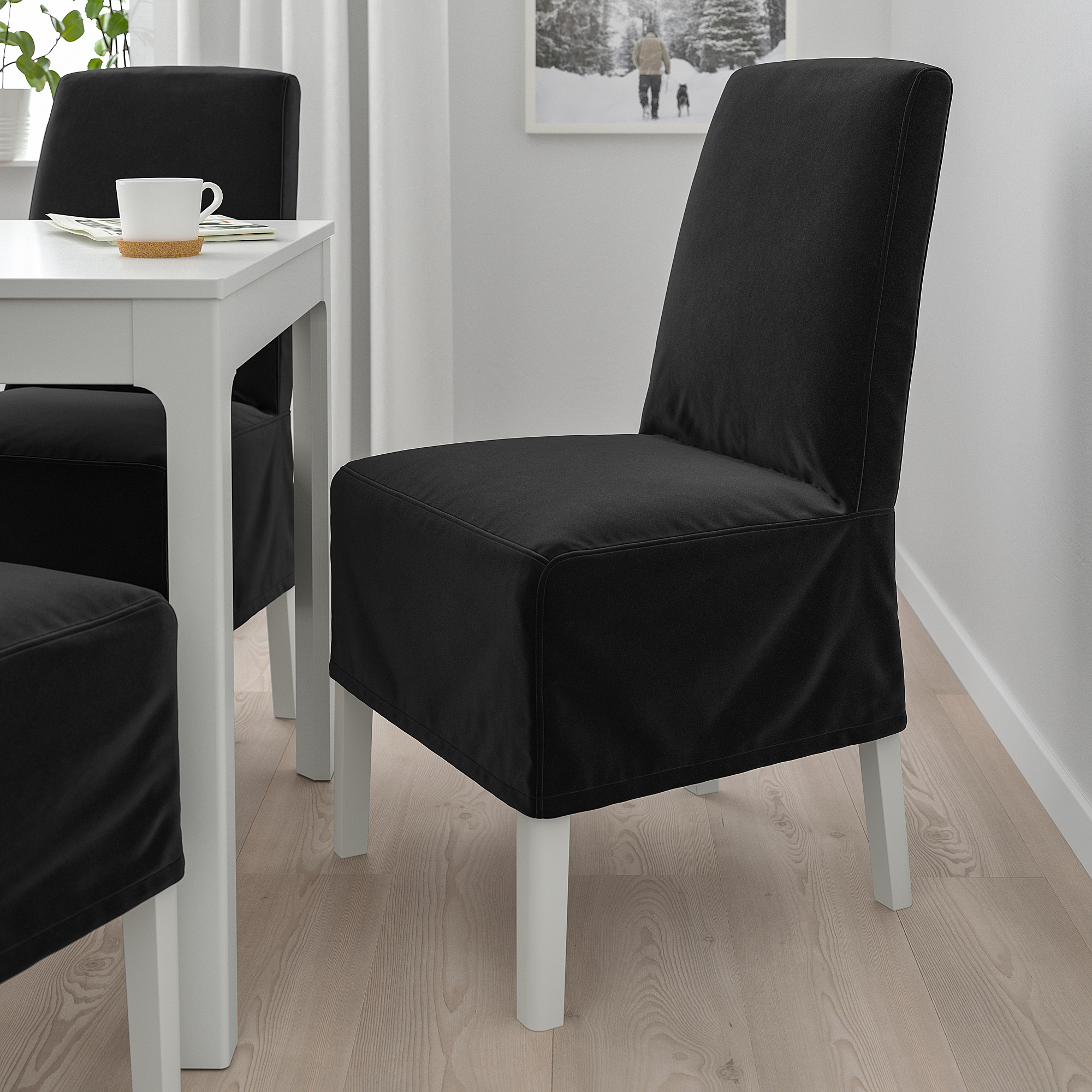 Zwei große schwarze BERGMUND Stühle mit Metallbeinen neben kleinem weißen Tisch mit Kaffeetasse.
