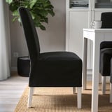 Schwarzer gepolsterter Stuhl mit Holzbeinen neben einem weißen Esstisch auf einem geflochtenen Teppich, der sein bequemes und stilvolles Design zur Geltung bringt.