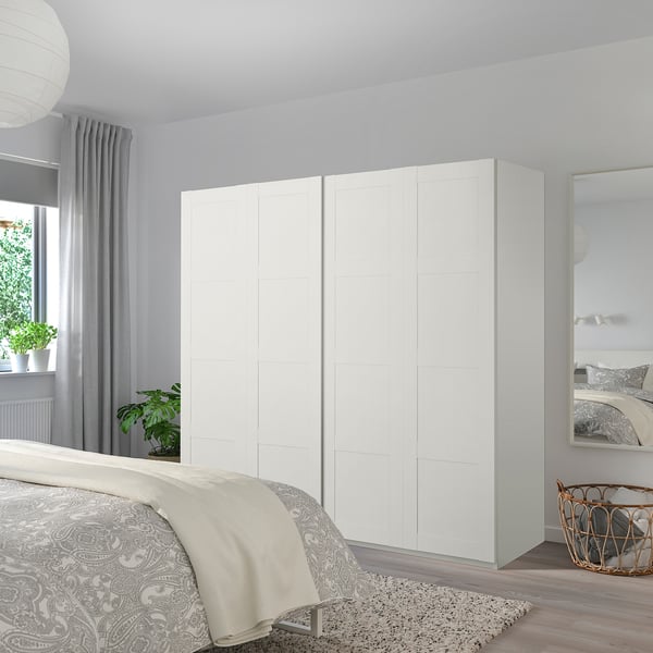 Minimalistisches Schlafzimmer mit großem weißem BERGSBO-Kleiderschrank und Schiebetüren neben dem Bett mit gemusterter Bettdecke an hellgrauer Wand.