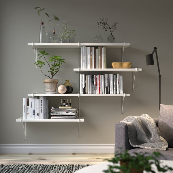 Minimalistisches Wohnzimmer mit weißem Regal, Büchern, Pflanzen, Lampe und Couch.