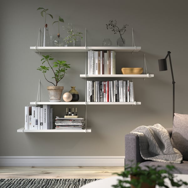 Modernes Wohnzimmer: weiße BERGSHULT Regale mit Büchern, Vasen, Pflanzen. Graue Wand, Couch, Lampe.