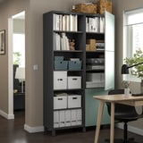 Modernes Homeoffice mit BESTÅ-Aufbewahrungsschrank in Dunkelgrau mit offenen Regalen und Schranktüren, in dem Bücher, Kisten und Dekorationsartikel untergebracht sind.