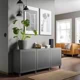 Modernes Wohnzimmer mit grauem BESTÅ-Stauraum, Pflanze, schwarzen Lampen, gerahmter Kunst, orangefarbener Couch, Holzboden und Teppich.