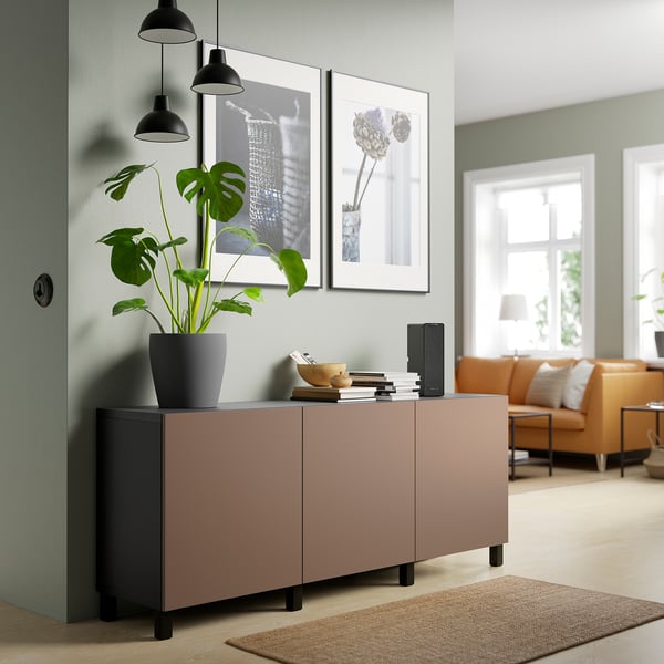 BESTÅ Sideboard aus hellem Holz mit Schubladen, Büchern, Lautsprechern, Pflanzen und Pendelleuchten.