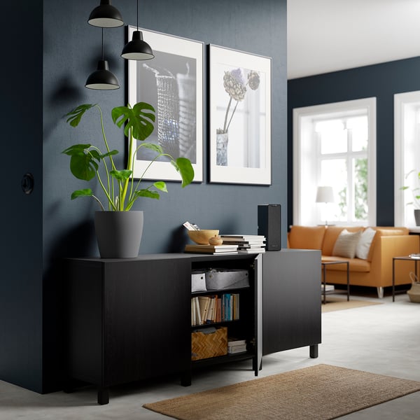 Modernes Zimmer mit dunkelgrauen Wänden, BESTÅ Sideboard, Pflanze, Büchern, Lautsprecher und beleuchteten Kunstwerken.