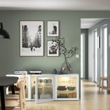 Moderner Essbereich mit BESTÅ Sideboard mit Glastüren, Geschirr und gerahmten Kunstwerken und einer Glasvase mit Zweigen dekoriert.