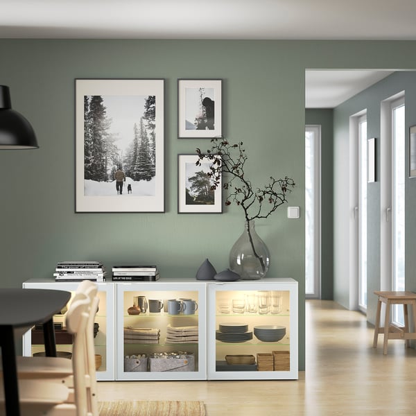 Modernes Esszimmer mit salbeigrünen Wänden, BESTÅ Sideboard mit Geschirr und Dekor, drei gerahmte Fotos.