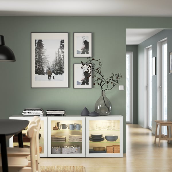 Modernes salbeigrünes Zimmer mit BESTÅ Sideboard, Kunstdrucken und Glasvase.