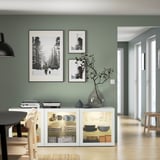 Modernes salbeigrünes Zimmer mit BESTÅ Sideboard, Kunstdrucken und Glasvase.