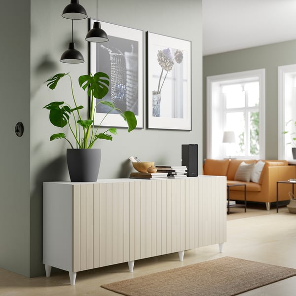 Modernes Wohnzimmer mit BESTÅ Sideboard, Pflanzen, Büchern, Pendelleuchten, orangefarbener Couch und beigem Teppich.