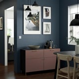 Dunkles BESTÅ Sideboard mit goldenen Griffen, Kunst und Lampen darüber, Stühle in der Nähe.