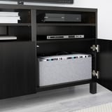 Schwarze BESTÅ-TV-Bank mit offener Tür, die Stauraum zeigt, darunter einen Laptop, elektronische Geräte und organisierte Kabel.