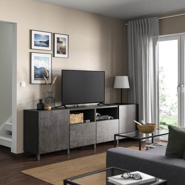 Modernes Wohnzimmer mit grauer BESTÅ-TV-Bank, Pflanzen und gerahmten Bildern. Holzböden und graue Vorhänge.