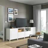 Modernes Wohnzimmer mit BESTÅ-TV, Flachbildfernseher, grauen Akzenten und Tageslicht. Sofa, Couchtisch und Lampe sind ebenfalls vorhanden.