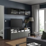 Modernes Wohnzimmer mit dunkelgrauer BESTÅ-TV-Bank, Wandschränken, Flachbildfernseher, Holzboden, großem Fenster mit Vorhängen, Tisch, Lampe und Couch.