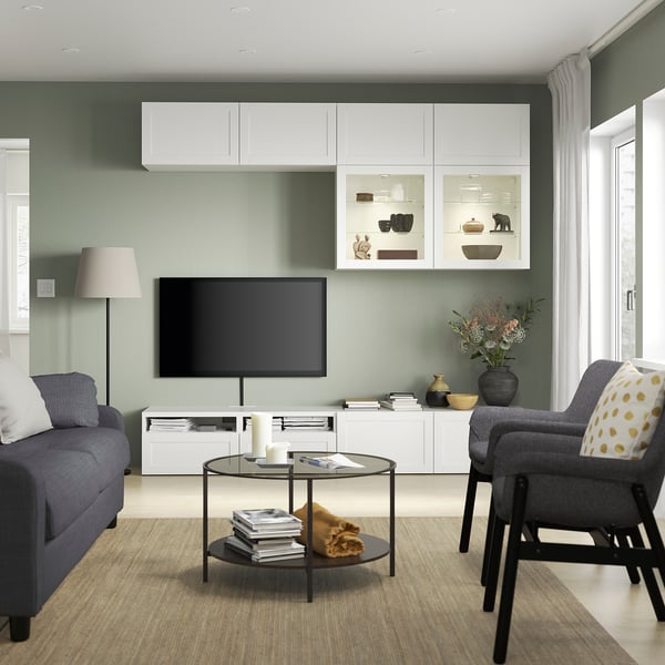 Modernes Wohnzimmer mit BESTÅ-TV, grauem Sofa und Couchtisch aus Glas. Wandregale bieten Platz für Dekoration und Bücher.