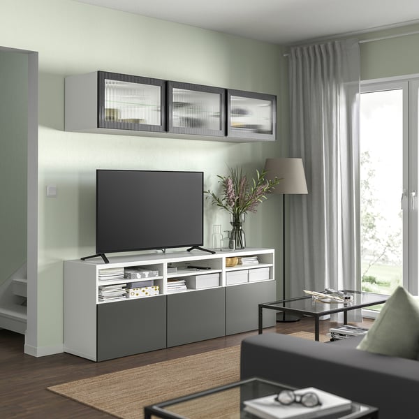 Modernes Wohnzimmer mit einer weiß-grauen BESTÅ-TV-Bank, einem Flachbildfernseher und Wandschränken mit Glastüren.