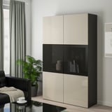 Moderner BESTÅ Aufbewahrungsschrank mit beigen und schwarzen Türen, hoch mit Gegenständen hinter Glas.