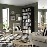 Modernes Wohnzimmer mit olivfarbenen Wänden, schwarzem Bücherregal BILLY hoch auf der rechten Seite, weißer Couch, gestreiftem Boden, Couchtisch und Uhr.