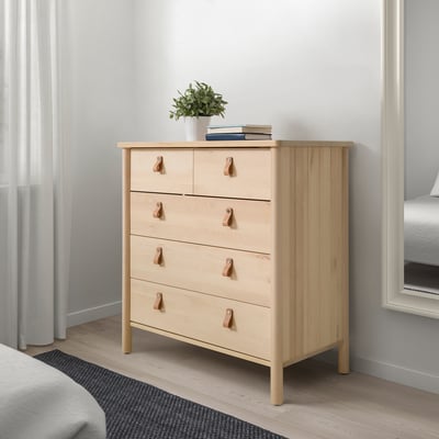 Kommode aus hellem Holz mit fünf Schubladen, Griffen und einer Vase obendrauf.