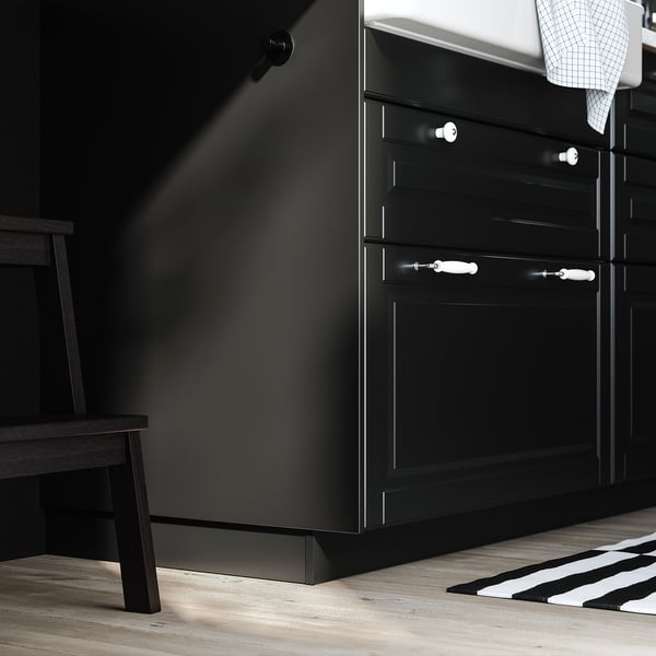 Schwarze Küchenschränke mit weißen Griffen und einem Holzhocker, modernes Design.