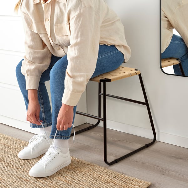 Person, die auf einem BOESKIL Jutehocker sitzt und weiße Turnschuhe bindet.