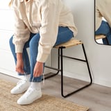 Person, die auf einem BOESKIL Jutehocker sitzt und weiße Turnschuhe bindet.