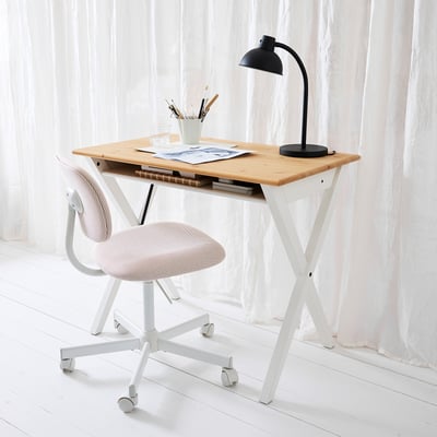 Ein blonder BOLLPOJKE-Schreibtisch mit Papieren, Lampe und Stuhl. Weiße Vorhänge erhellen den Raum.