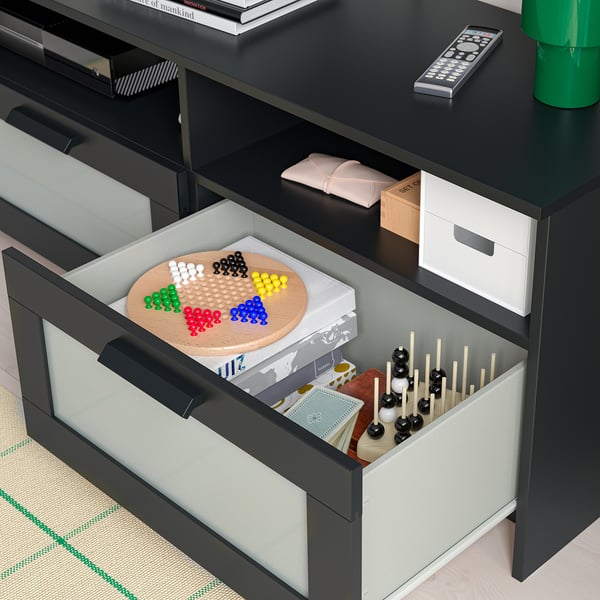 In der offenen Schublade sind Brettspiele, Spielsteine und Fernbedienungen zu sehen, die im TV-Ständer organisiert sind.