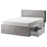 Ein graues BRIMNES-Bett mit vier Schubladen und einem hohen Kopfteil, ideal für kompakte Räume.