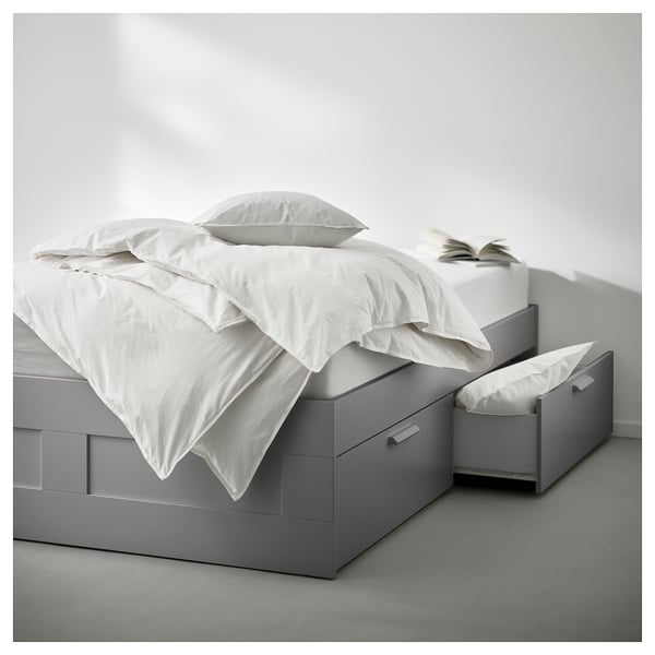 Minimalistisches graues Bett BRIMNES mit 4 Schubladen, weißer Bettwäsche, modernes, stauraumfreundliches Design.