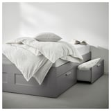 Minimalistisches graues Bett BRIMNES mit 4 Schubladen, weißer Bettwäsche, modernes, stauraumfreundliches Design.