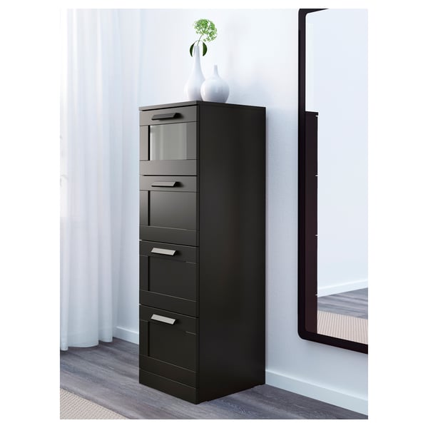 Schwarzer Hochschrank mit Glasschublade, drei zusätzlichen Schubladen und einer Vase obendrauf.
