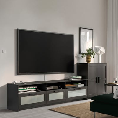 Modernes Wohnzimmer mit großer schwarzer BRIMNES-TV-Bank und Schrank. Fernseher zentral platziert, flankiert von Dekor und Büchern. Grünes Sofa an der Seite.
