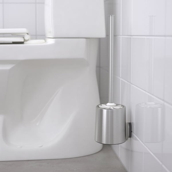 Bürstenhalter aus Metall, der an einer gefliesten Wand befestigt ist und eine weiße Bürste hält, neben einem weißen Waschbecken. Teil der BROGRUND-Serie für aufgeräumtes Bad.