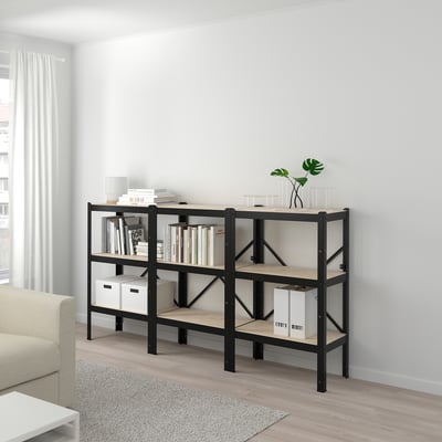 Modernes Wohnzimmer BROR schwarz-beiges Bücherregal mit Büchern, Kisten und Pflanzen. Es ist groß, robust und passt gut unter ein Fenster.