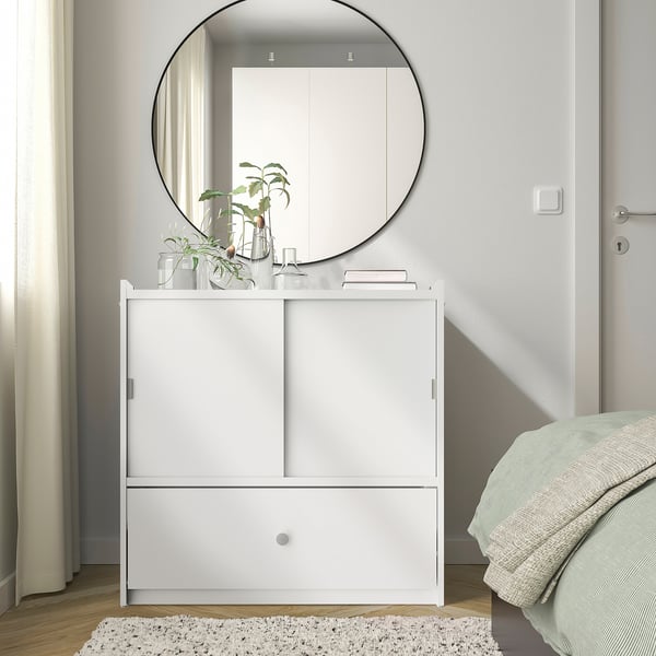 Modernes Schlafzimmer mit weißer BRUKSVARA-Truhe, Spiegel, Pflanzen und weicher Bettwäsche. Kompaktes und dennoch geräumiges Design.