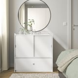 Modernes Schlafzimmer mit weißer BRUKSVARA-Truhe, Spiegel, Pflanzen und weicher Bettwäsche. Kompaktes und dennoch geräumiges Design.