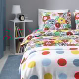 Bunte Blumenbettwäsche, weiße Kissen, Nachttisch mit Lampe, Bücher und Uhr.