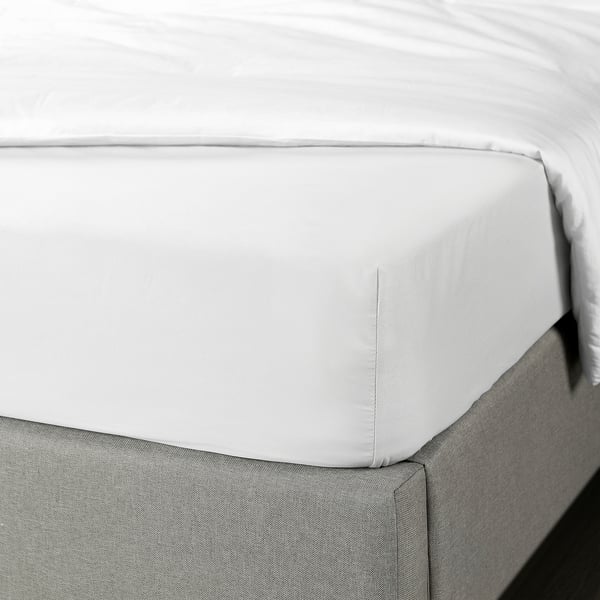 Frisches, weißes Spannbetttuch auf dem Bett, umschließende Matratzenkante mit Gummiband für sicheren Sitz.