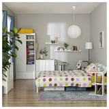 Modernes Schlafzimmer mit weißen Möbeln, buntem Bett und Pflanzen.