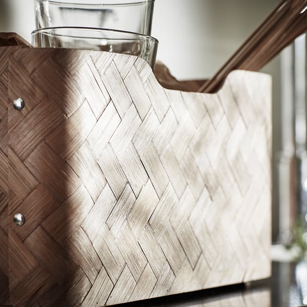 Natürlicher Weidenkorb mit klarem Glasgefäß, auf Holzregal gestellt.