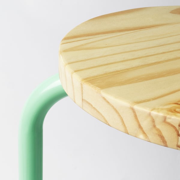 Runder Holzhocker mit glatter, heller Sitzfläche auf grünen Metallbeinen.