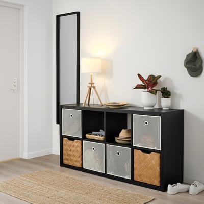 Kallax Regal mit DRÖNJÖNS Boxen. Lampe, Pflanzen, Hut und Turnschuhe ausgestellt.