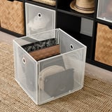 Aufbewahrungsbox aus Mesh mit offener Front, die Gegenstände im Inneren freigibt, platziert auf einem gewebten Teppich. Perfekt zum Organisieren und einfachen Zugriff auf Gegenstände.