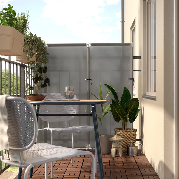 Moderner Balkon mit weißem Metalltisch und Stühlen, umgeben von üppigen grünen Pflanzen, die einen ruhigen Außenbereich schaffen.