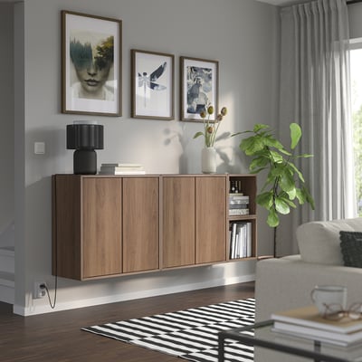 Modernes Wohnzimmer mit wandmontierten EKET-Schränken, Büchern und Dekor. Kunst, Pflanzen, graue Vorhänge, gestreifter Teppich.