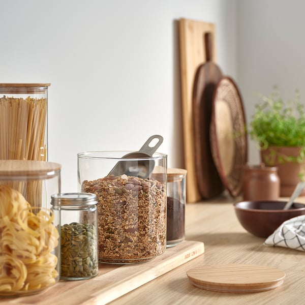 Küchentheke mit Müslidose, Bambusdeckel, umgeben von kleinen Gläsern, Holzbrettern und Kräutern.