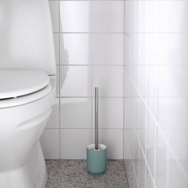 Minimalistisches Badezimmer mit weißer Toilette, blauem Bürstenhalter und grauer Bürste.