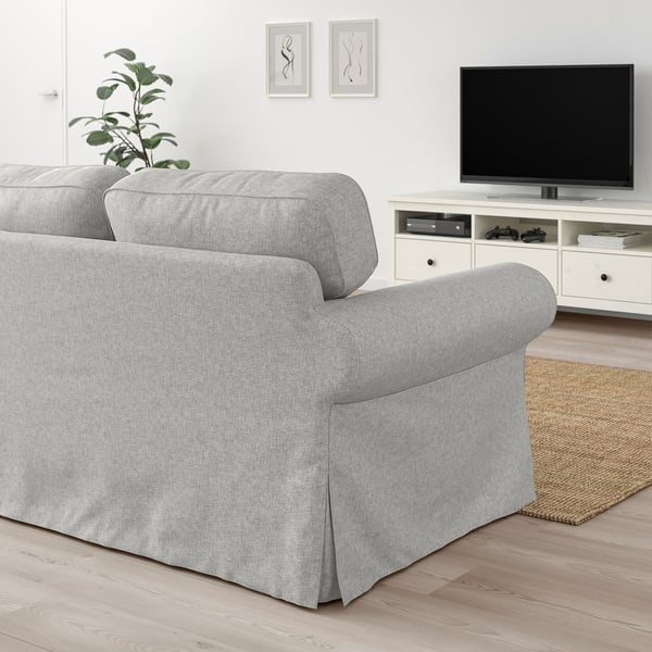 Helles Wohnzimmer EKTORP hellgraues Sofa, großer Fernseher, weißer Schrank, Juteteppich und Pflanze. Die Größe der Sofas dominiert den Raum und bietet Komfort.